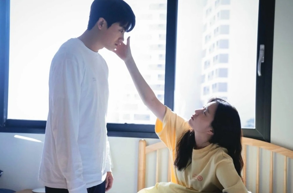 The romantic scene from the Happiness Korean drama where main female lead is laying on the sofa and putting her hand on the jaw of male lead