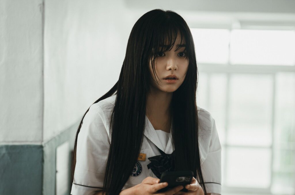 Kang Mi-na as Lim Na-ri in If Wishes Could Kill where she is sitting in uniform in classroom with mobile in her hand and scared of  something